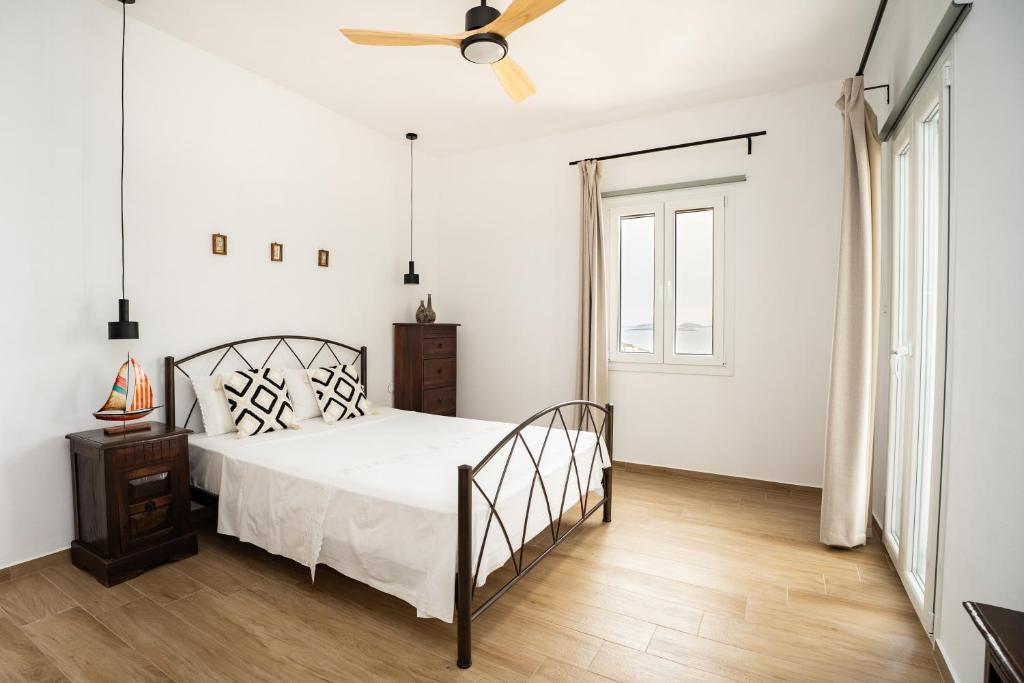 a white bedroom with a bed and a ceiling fan at Anemoessa House in Pera Gyalos