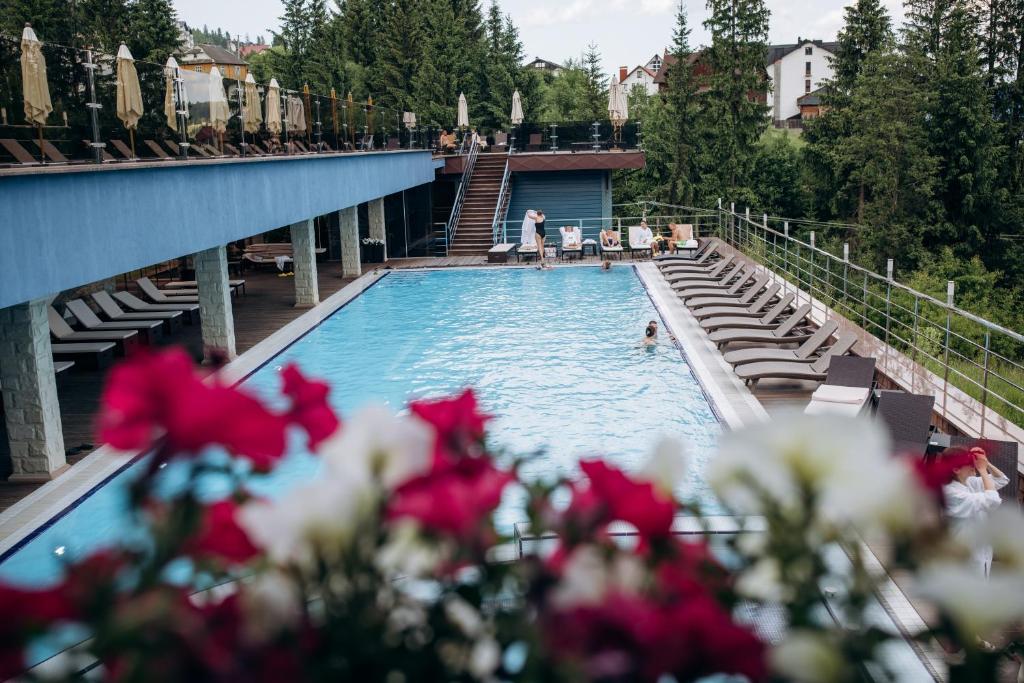 a swimming pool with red flowers in the foreground at Gasthaus & Spa Bukovel in Bukovel
