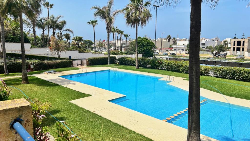 a large blue swimming pool with palm trees and grass at Spacious Triplex in Harhoura in El Harhoura