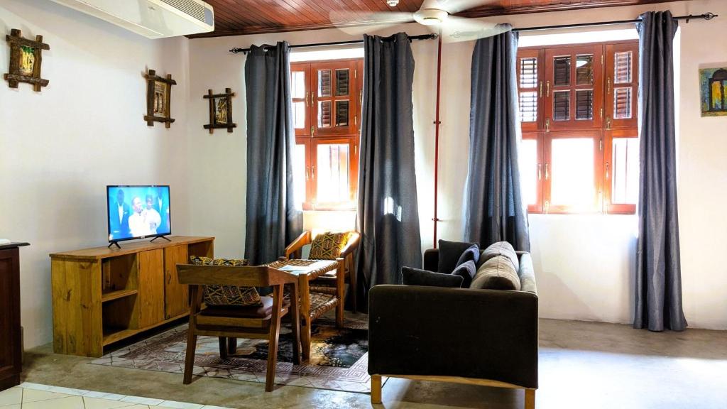a living room with a couch and a table and windows at Kays Place Train house Jambo in Zanzibar City