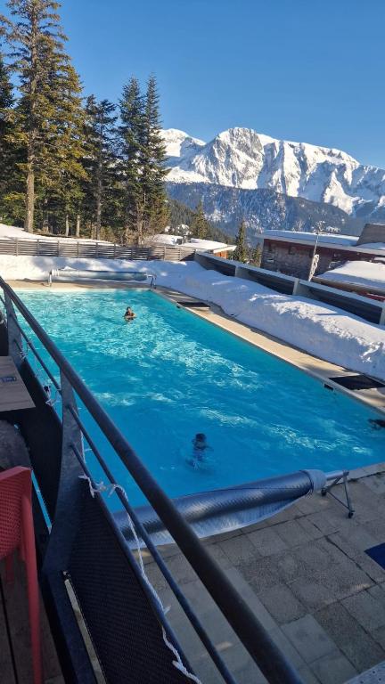 two people swimming in a swimming pool with snow covered mountains at DFJ des Neiges, Piscine, Pieds des pistes in Chamrousse
