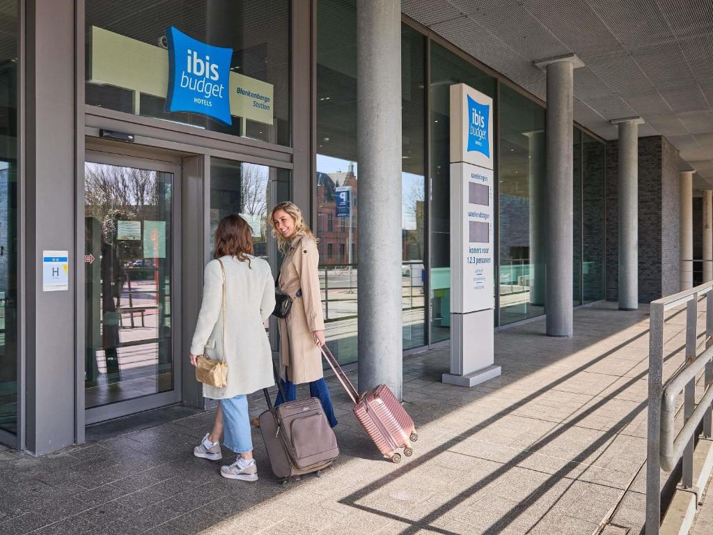 two women standing outside of a building with luggage at ibis budget Blankenberge in Blankenberge
