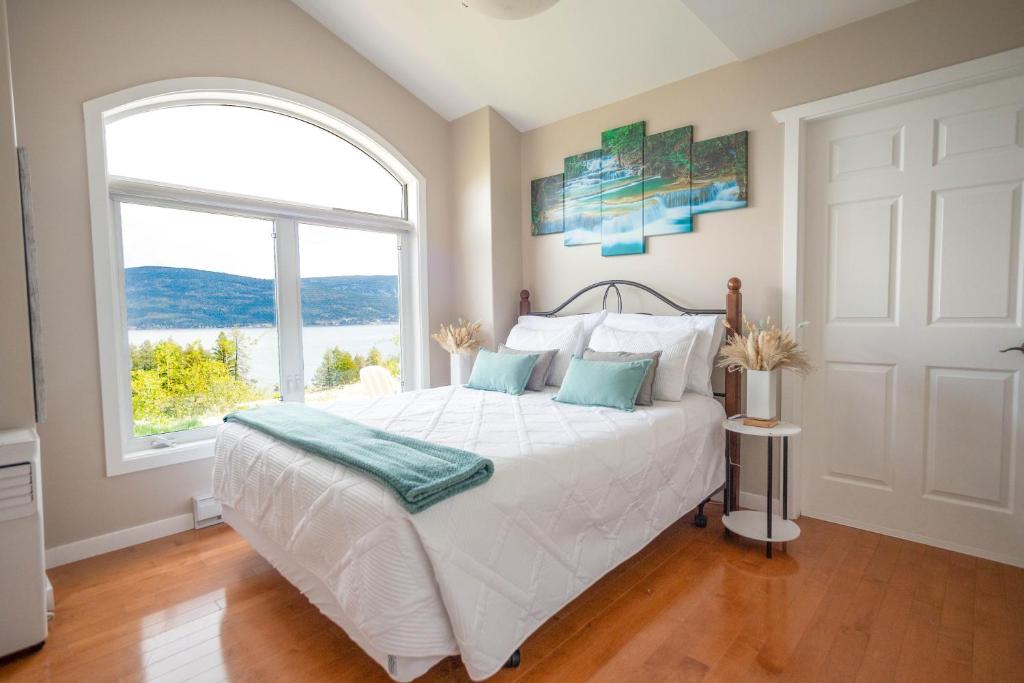 a bedroom with a white bed with a large window at Panoramic Acres B & B - Lake & Mountain Views in Vernon