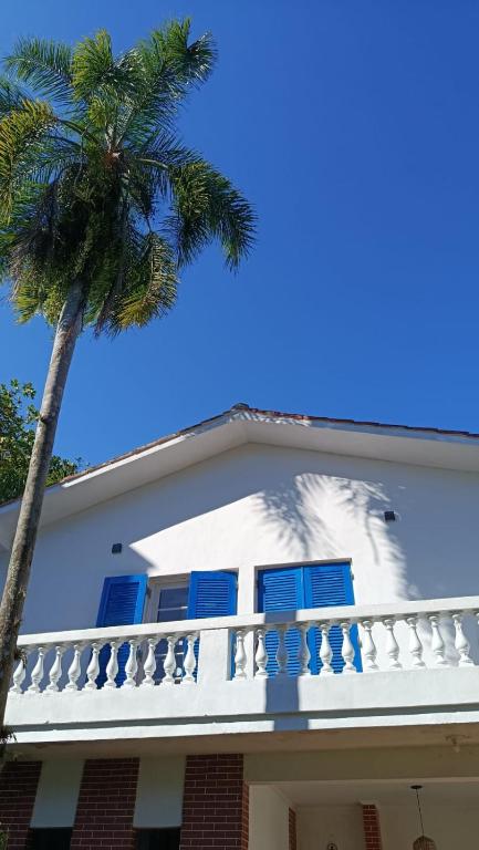 a white house with a palm tree at Casa Pé na Areia Cantão do Bora Bora - Manaaki Surf Hostel in São Sebastião