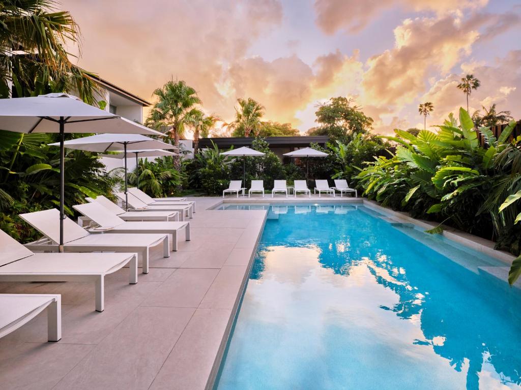 an infinity pool with white lounge chairs and umbrellas at The Hide Byron Bay in Byron Bay