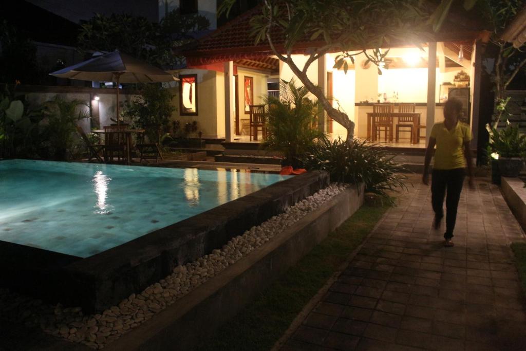 a woman walking by a swimming pool at night at Puri Clinton Bali in Nusa Dua