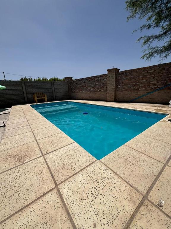 a swimming pool with blue water in front of a brick wall at Los Girasoles in Albardón