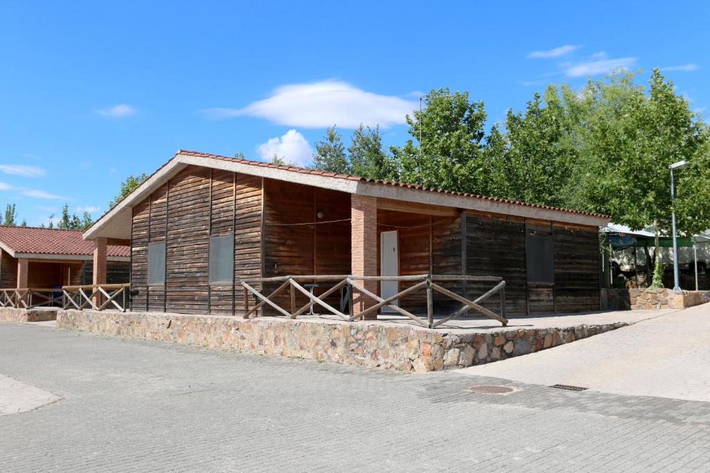 una pequeña casa de madera con una pared de piedra en Hostal - Bungalows Camping Cáceres, en Cáceres