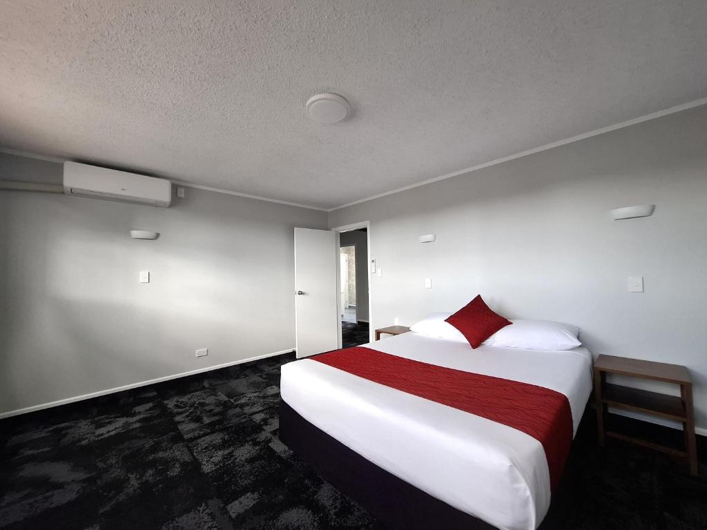 a bedroom with a large white bed with a red pillow at Beetham Park Motel in Hamilton