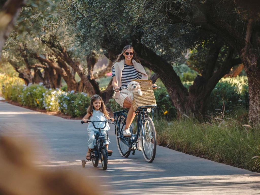 a woman and a child riding a bike with a dog in a basket at Fairmont Royal Palm Marrakech in Marrakesh