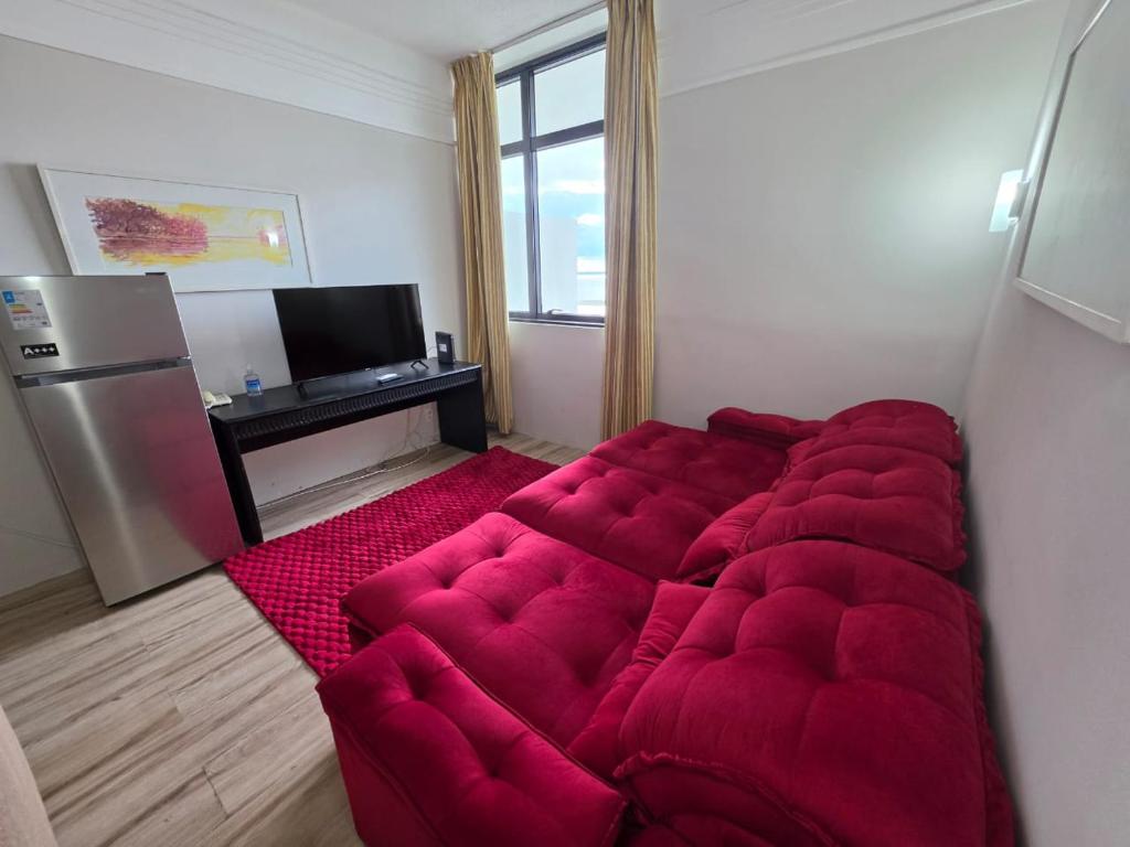 a large red couch in a room with a refrigerator at Suíte com varanda Tropical Hotel in Manaus