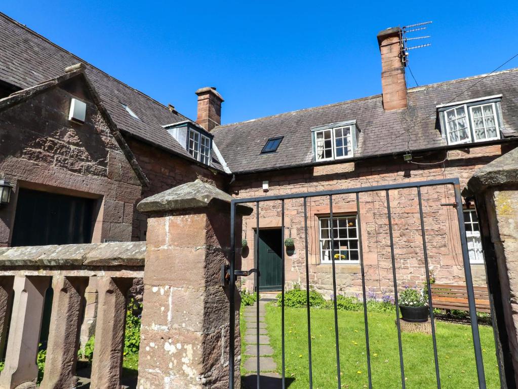 an old brick house with a fence at Gamekeepers Cottage in Chillingham