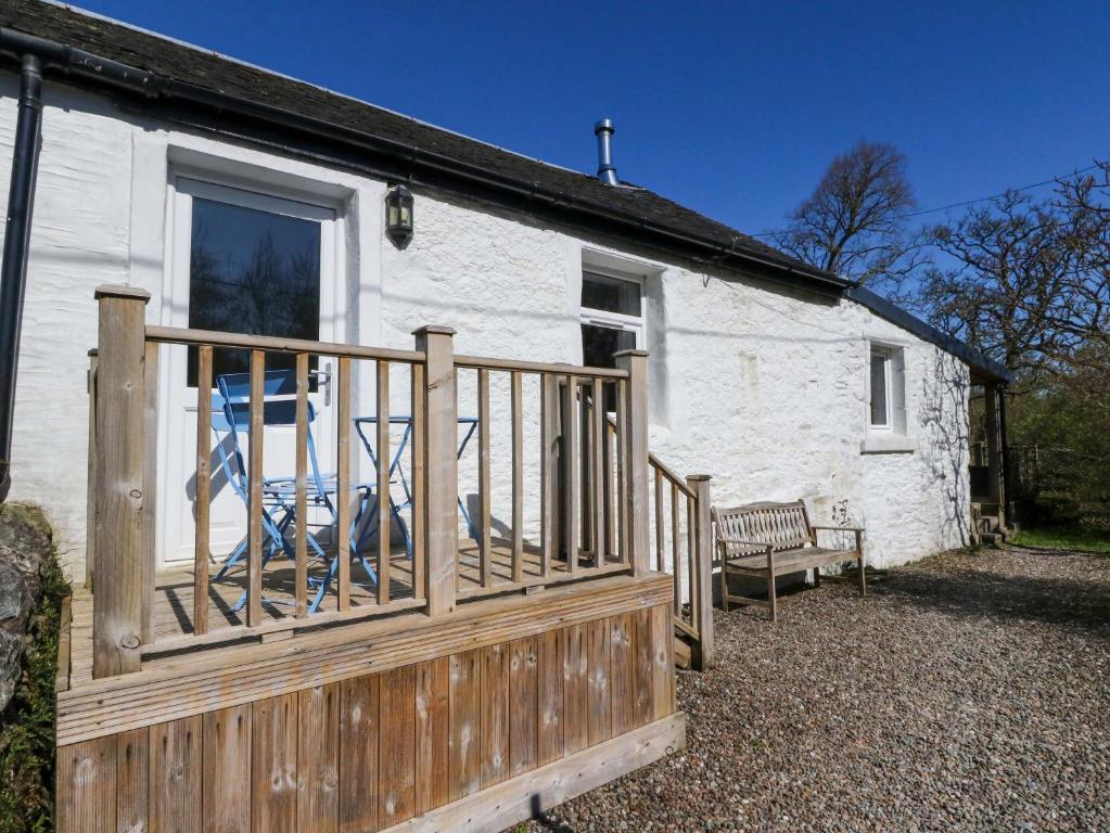 a white house with a wooden porch and a bench at Gun Powder Cottage in Tighnabruaich