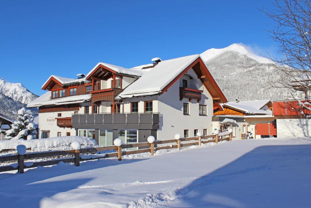 a house in the snow with mountains in the background at Appartementhotel Zugspitzhof in Ehrwald