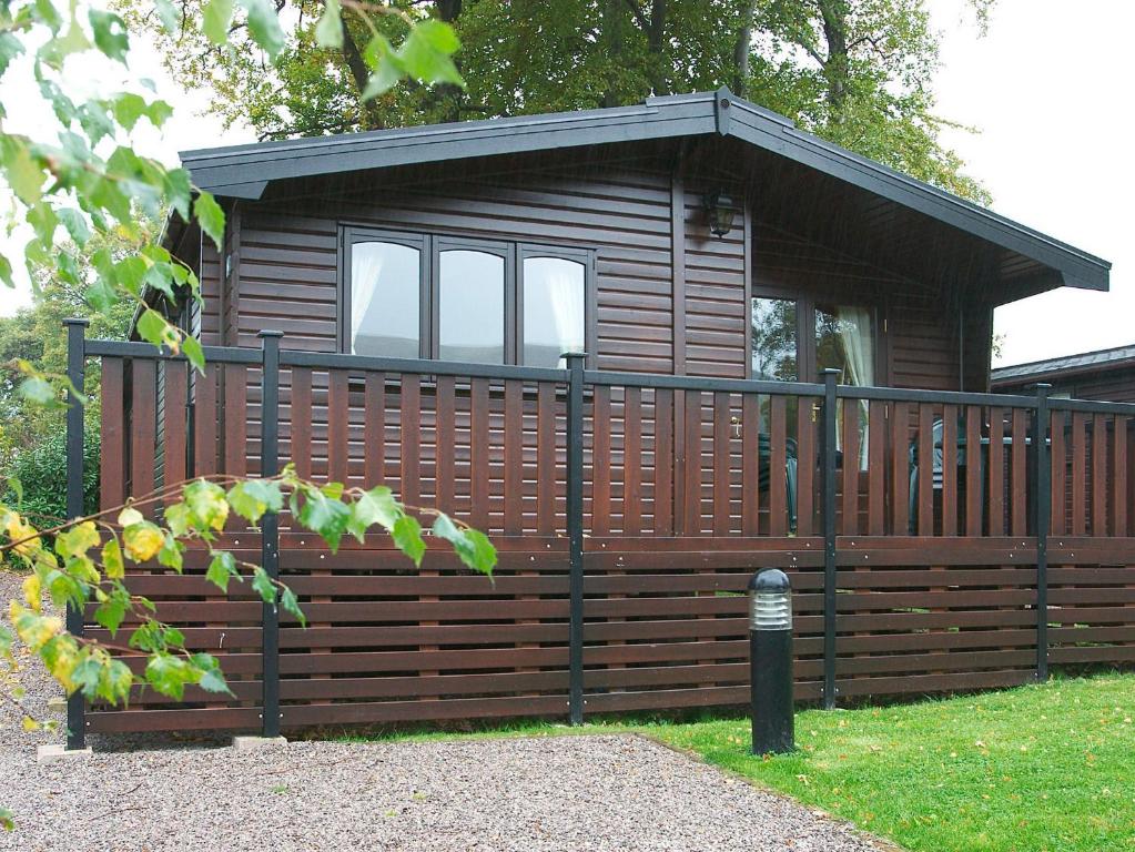 a wooden cabin with a fence in the grass at Burnside Park in Keswick