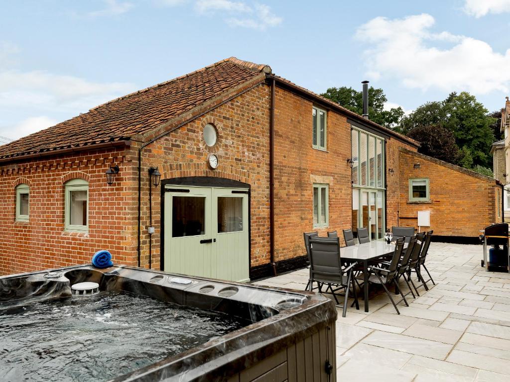 a patio with a hot tub in front of a brick building at Pipistrelle Barn in North Walsham