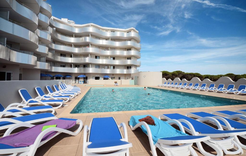 a swimming pool with lounge chairs and a building at Résidence Odalys Le Lotus Blanc in Le Barcarès
