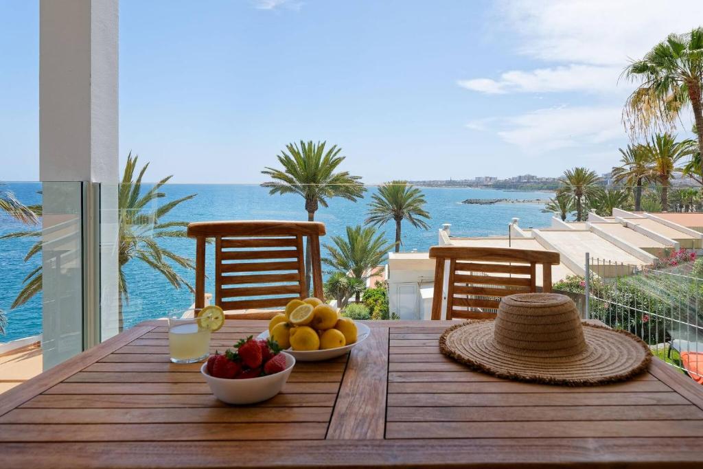 a wooden table with a bowl of fruit and a view of the ocean at Deva Beach Boutique Apartments in San Bartolomé