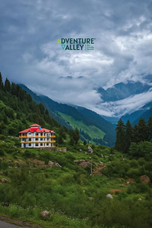 a building on a hill in a field with mountains at Adventure valley Rajgundha in Kangra