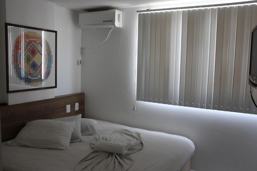 a white bedroom with a bed with a window at Ametista Flat in Maceió