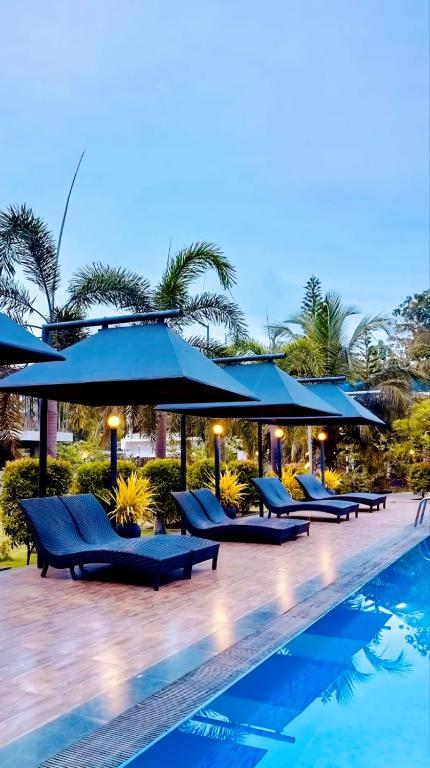 a pool with blue lounge chairs and umbrellas at Hotel Green Garden PVT LTD in Trincomalee