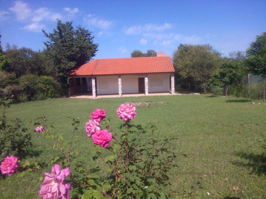 una pequeña casa en un campo con flores rosas en Casa soñada con vista a la Sierra de los Comechingones en Merlo