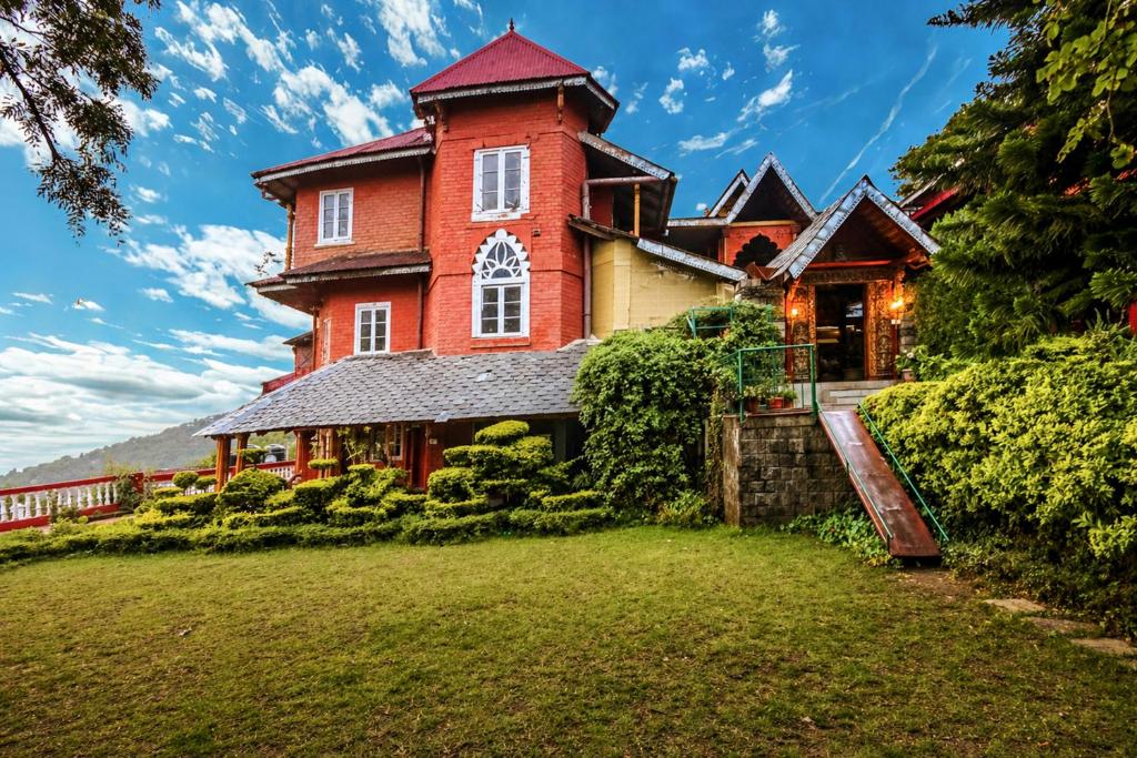 a large red brick house on a hill with a yard at WelcomHeritage Grace Hotel in Dharamshala