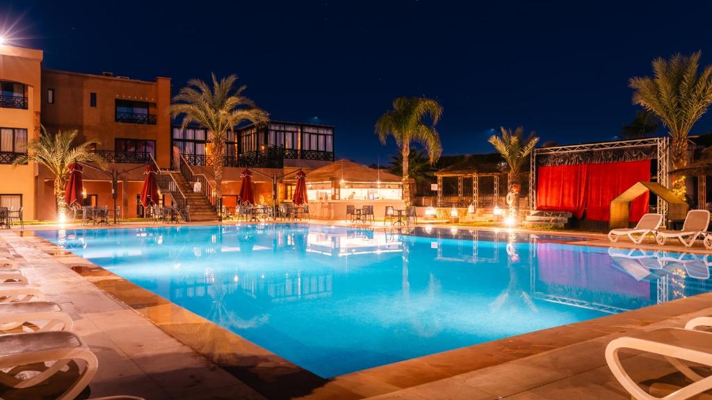 a large swimming pool at night with palm trees and buildings at Club Paradisio in Marrakesh