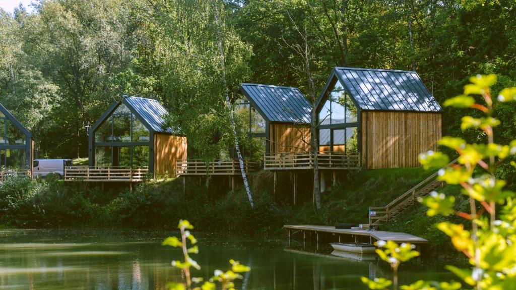 three houses on the shore of a lake with trees at Leśne Szepty Resort in Zebrzydów