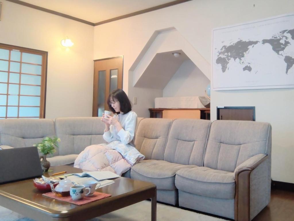 a woman sitting on a couch looking at her cell phone at 民泊よこてこよ in Yokote