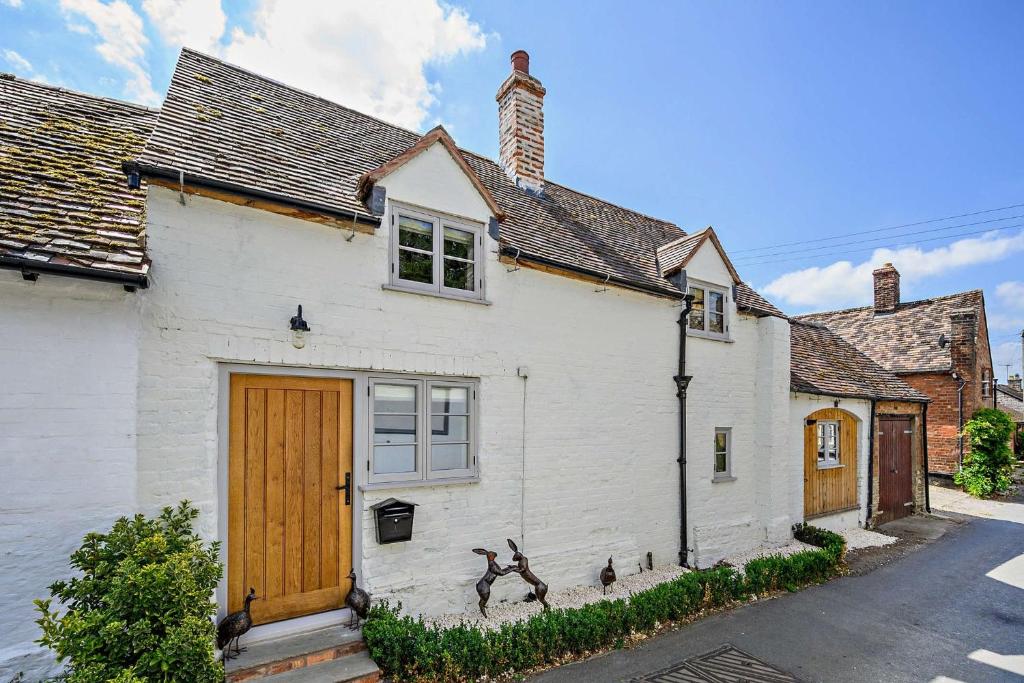a white house with a brown door and some buildings at March Hare Cottage in Bretforton in Bretforton