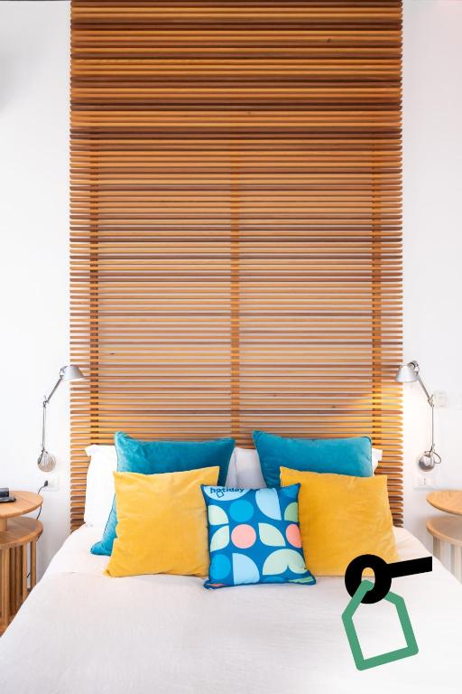 a bed with yellow and blue pillows and a wooden headboard at Hotiday Torre Lapillo Centro in Torre Lapillo