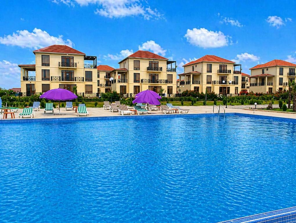 a swimming pool in front of a resort with purple umbrellas at Delmar Boutique Buzovna in Mekhrably