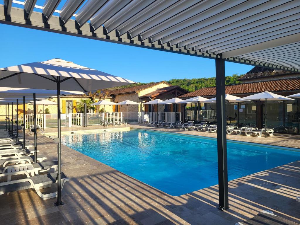 a swimming pool with umbrellas and chairs at L'Oustal de Vézac in Vézac