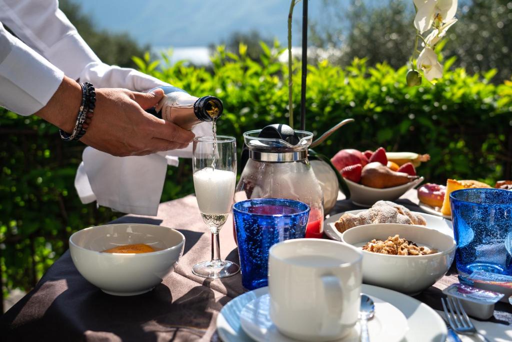 a person pouring a glass of milk on a table with food at Hotel Silvana Garnì in Limone sul Garda