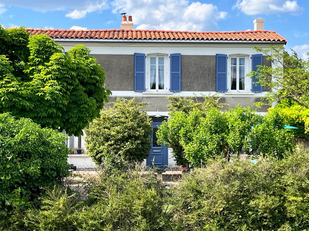 a house with blue shutters and trees at La Cachette de Beaumont in Marsais