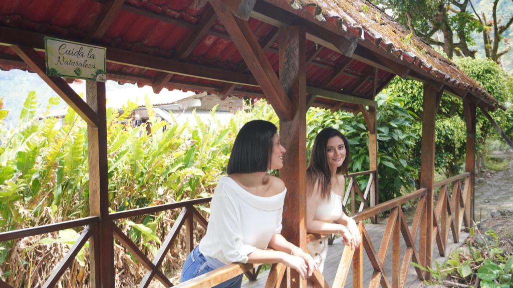 two young women sitting on a wooden bridge at Monte Selva Hotel Spa Termal in Baños