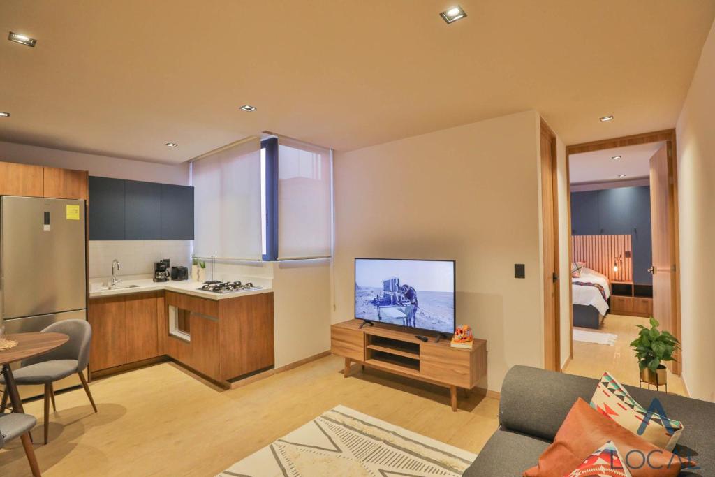 An open-plan studio living area with a kitchenette, television, sofa and visible bedroom beyond.