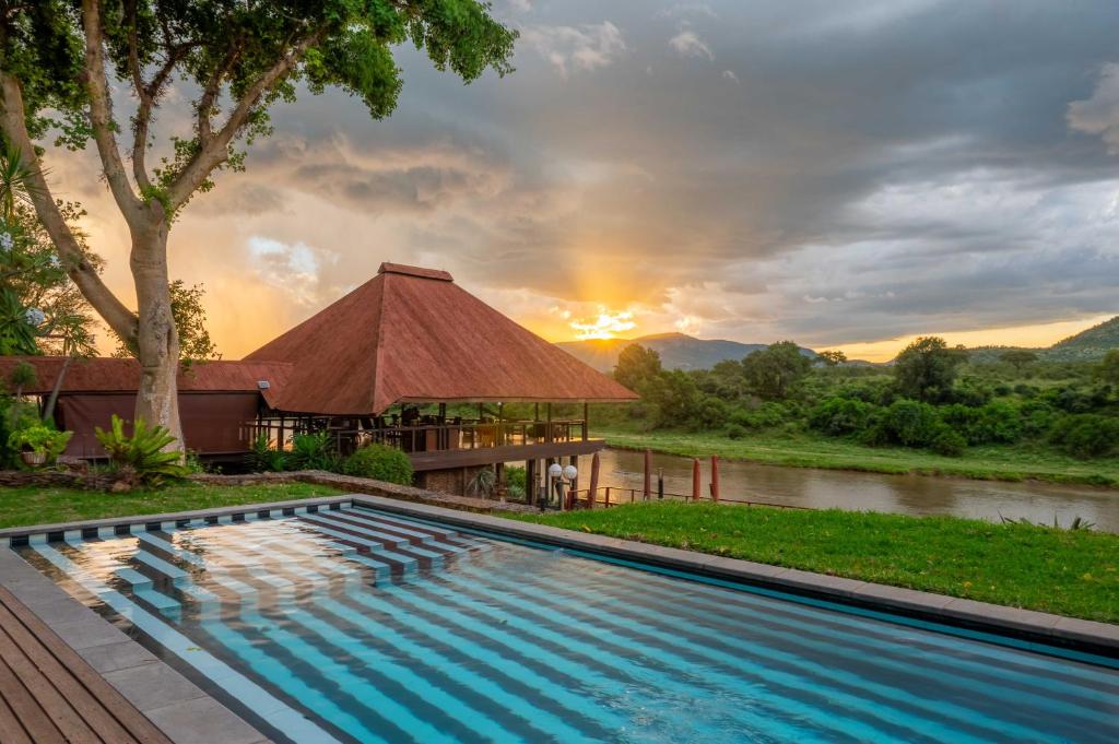 a swimming pool in front of a house with a sunset at River House Lodge in Malelane