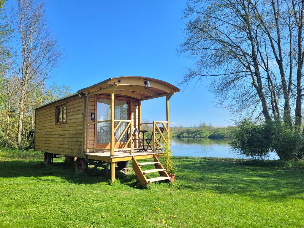 a tiny house sitting in the grass next to a lake at La Roulotte du Marais in Éclusier-Vaux