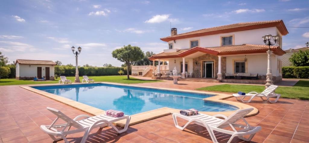 a house with a swimming pool and two lawn chairs at Casa Rural Los Gaspares in La Carlota