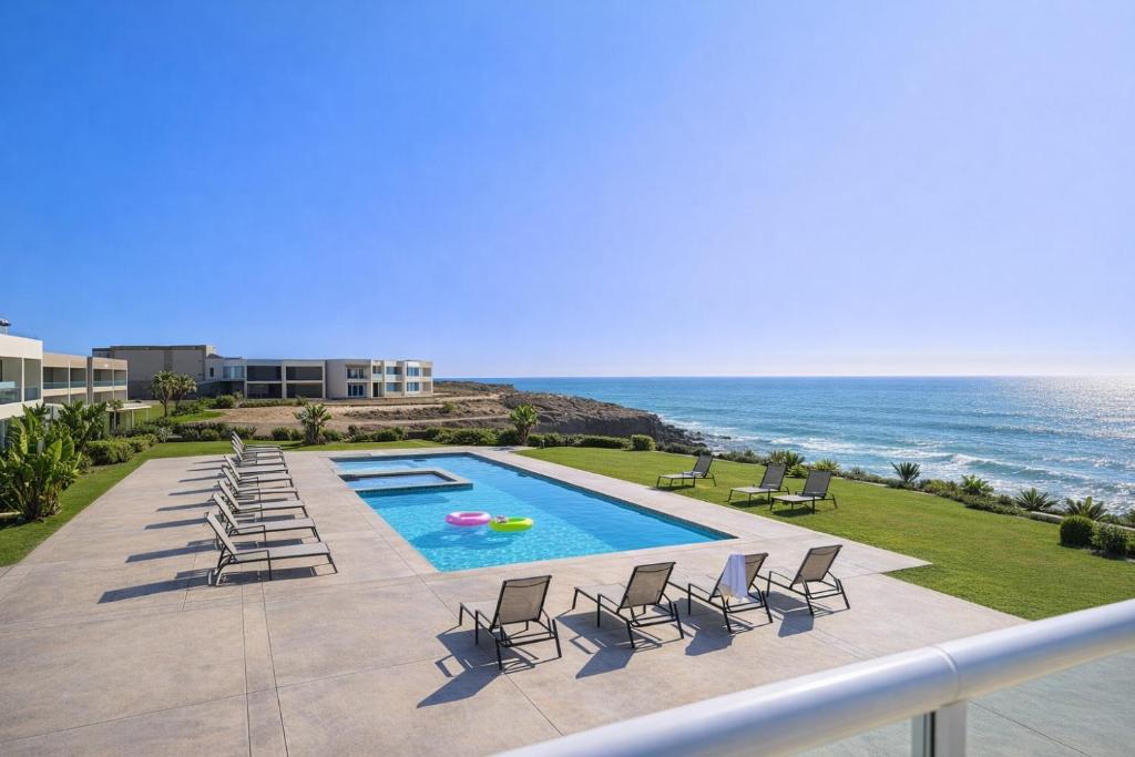 a view of a swimming pool with chairs and the ocean at Panoramic Oceanfront Resort Style Condo in Rosarito