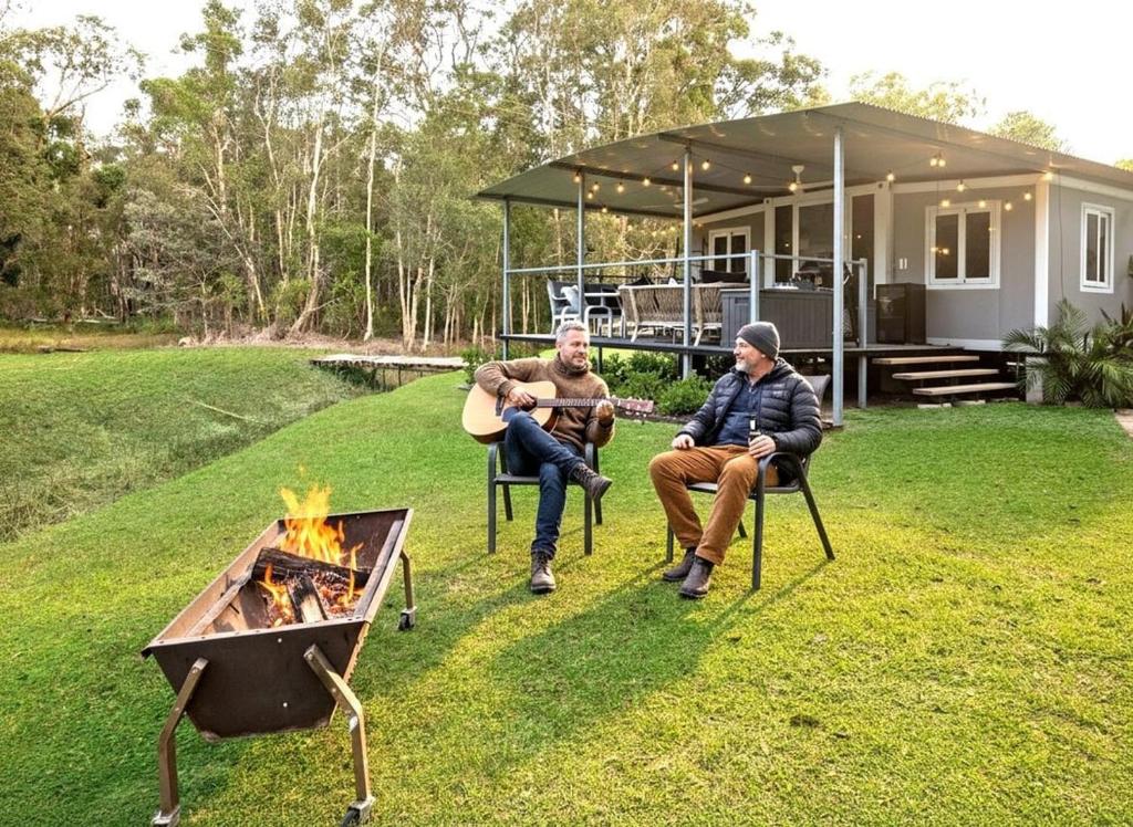 two men sitting around a fire pit in front of a house at Leo's Beach Hideaway - Stylish Tiny Home in Arrawarra