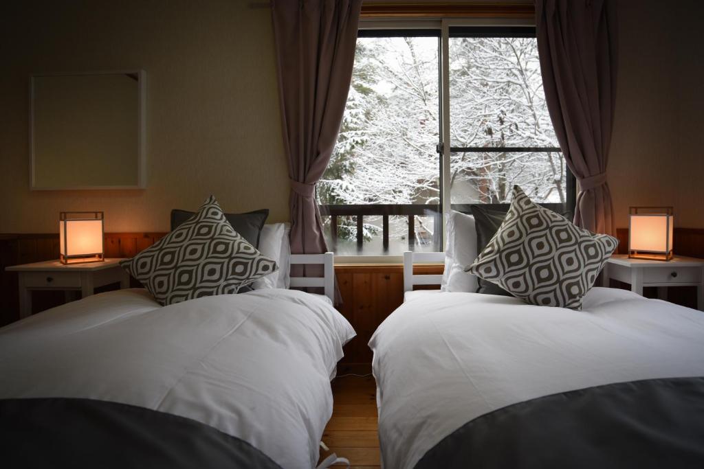 two beds in a room with a window and two lamps at Sheltered Inn Hakuba in Hakuba