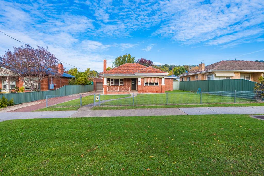 a house with a fence in front of a yard at Red Brick Beauty - Central Cottage in Albury