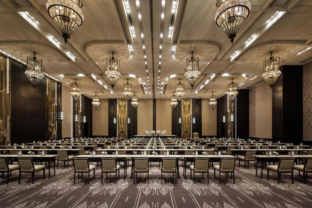 A very large formal ballroom arranged in long rows beneath ornate chandeliers.