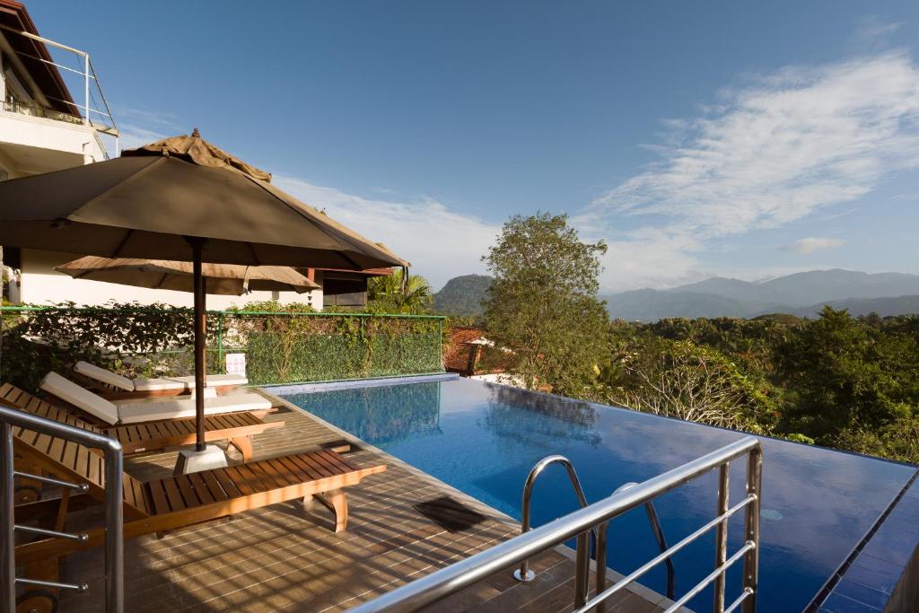 a swimming pool with an umbrella and benches next to at Villa Subashri, Victoria Golf Greens - Digana in Kandy