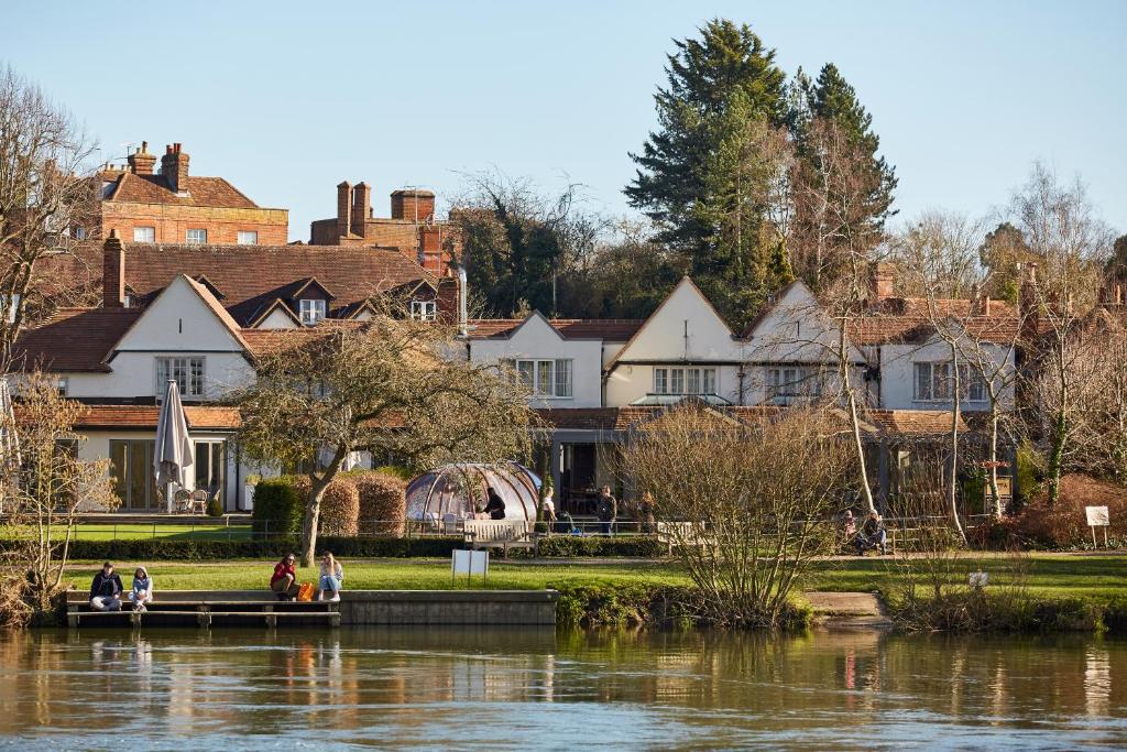 a group of people sitting on the grass near a lake at The Great House, Sonning, Berkshire in Reading