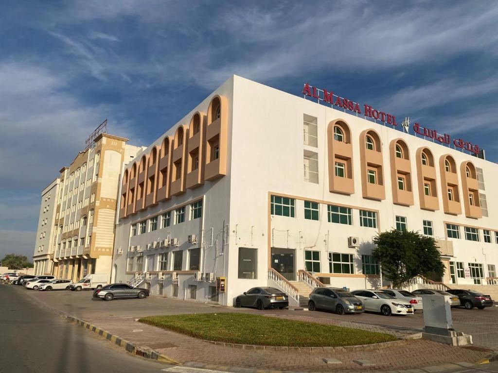 a large white building with cars parked in a parking lot at Hotel Al Masa in Al Buraymī