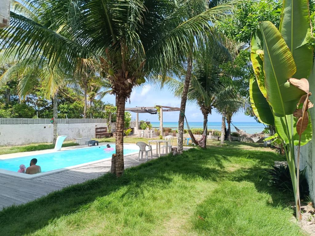 a pool with palm trees and people sitting in it at Suites Dupla beira mar Carapibus in Conde